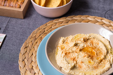 Tasty hummus chickpea food sauce on a plate on a blue and grey fabrics dinner table on a black background