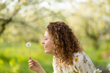 Pretty girl blowing dandelion in summer park. Green grass beautiful nature. Pure emotion.