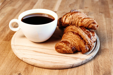 Cup of black freshly brewed coffee. Crispy croissant, breakfast in cafe.