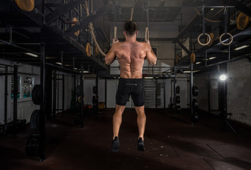 Young active strong sweaty athlete muscular fit man with big muscles doing cross workout training on the gymnastic rings for hole body dip for abs hands and back in the gym