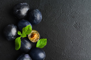 Blue fresh organic plums with mint over black textured background