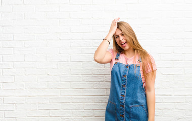 young blonde woman laughing and slapping forehead like saying d‚Äôoh! I forgot or that was a...