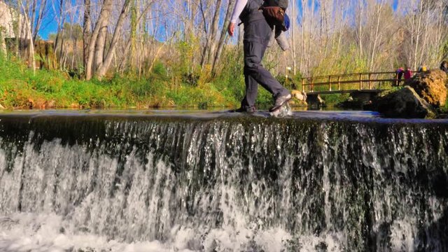 Senderista caminando sobre las aguas de r&iacute;o junto a cascada de agua