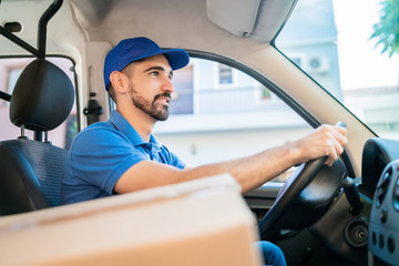 Delivery man driving van with cardboard boxes on seat.
