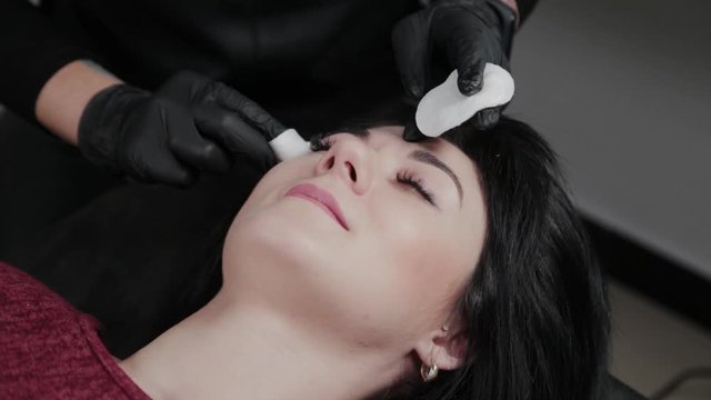 Professional permanent makeup master removes makeup from the face with cotton pads to the client.