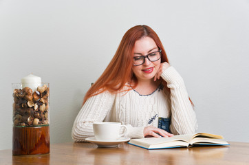 A woman with freckles drinking coffee and reading a book