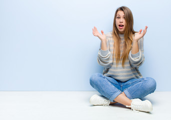 young blonde woman feeling shocked and excited, laughing, amazed and happy because of an unexpected...