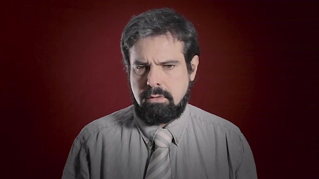 An alienated man's expression. Medium close-up shot of the face over a red background. Part of a series of depictions of feelings and emotions with professional actors.