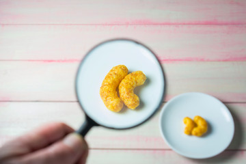 Corn snacks in a small plate magnified by a magnifying glass.