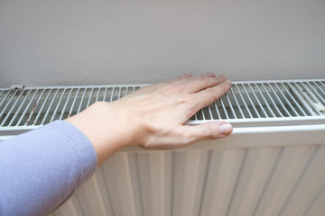 A hand touching white radiator of a central heating system, checking the temperature of a heater,...