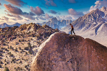 Man rock climbs on huge granite boulder in the Buttermilk area of Bishop, California with the Sierra Nevada  behind - obrazy, fototapety, plakaty