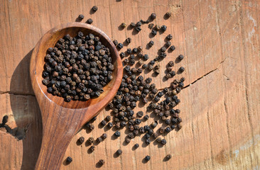 Black peppercorns in wooden spoon on wooden background