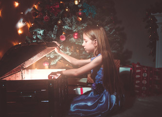 Little girl on the floor near the Christmas tree at Christmas with a magic glowing chest with gifts