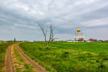 Fototapeta na wymiar Orthodox church on a background of green field and stormy clouds