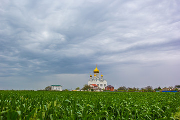 Orthodox church on a background of green field and stormy clouds