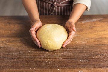 Pair of hands holding a light yellow bread dough on wood surface table top.
