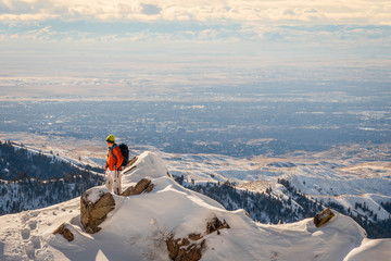 Backpacker on top of a snowy mountain overlooking the city.