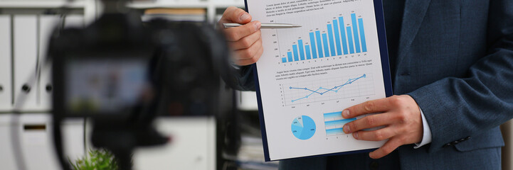 Male in suit and tie show stats graph pad making promo videoblog or photo session in office camcorder to tripod closeup. Vlogger selfie sale solution or finance advisor management information © H_Ko
