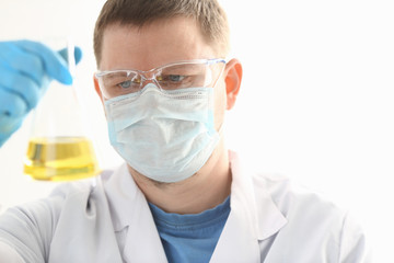 A portrait of a young surgeon chemist doctor looks at a container with a yellow liquid and a mask is fought with viruses and a vaccine for vaccines against diseases.