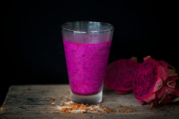 Red Dragon fruit juice on wooden surface, solid black background, still life shooting style.