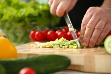 Cook holds knife in hand and cuts on cutting board green onions for salad or fresh vegetable soup with vitamins. Raw food and vegetarian recipe book in modern society popular concept.