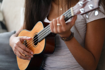 Fototapeta premium Close-up of latino woman holding ukulele and learning how to play. Young female exercising in playing. Musical wooden instrument. Music and art concept