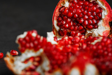 Juicy seeds of fresh fruit of the opened pomegranate on a black background close-up.