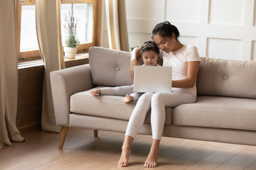 Fototapeta premium Young ethnic mom and little daughter use computer together
