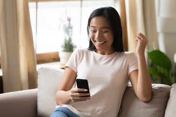 Overjoyed Asian girl triumph reading good news on cell