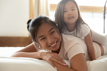 Happy Asian mother and small daughter cuddle in bed