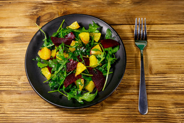 Tasty salad of fresh arugula, beetroot and oranges on wooden table. Top view. Healthy food or vegetarian concept