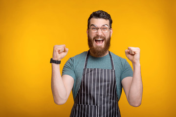 Photo of amazed bearded chef man celebrating over yellow background