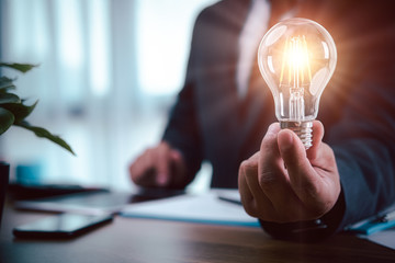 businessman hand holding light bulb with finance document and tool,concept of New ideas for business and fonance. - Powered by Adobe