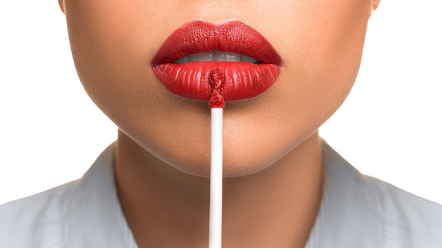 Young woman applying a lip gloss on her lips on white background.
