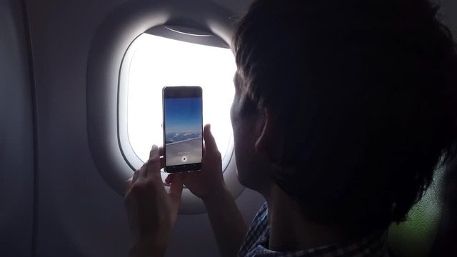 Young man takes a picture on the phone of a view from the airplane window in flight