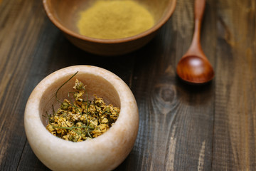 Marble mortar with dried chamomile for natural cosmetics. Clay bowl with yellow powder or clay and flowers on a wooden background. Flat lay