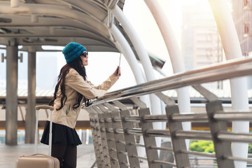 Traveler young woman wearing green hat and sunglasses with suitcase holding tablet in her hands directions searching something while alone standing in the city. Travel tourism, technology concept.