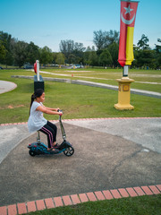 A nice Asian young girl is riding a scooter. Active leisure in the park. Children's sports