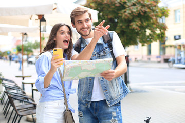 Beautiful young couple holding a map and smiling while standing outdoors.
