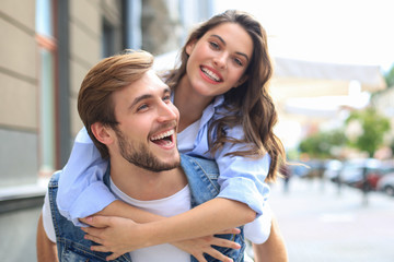 Handsome young man carrying young attractive woman on shoulders while spending time together outdoors.