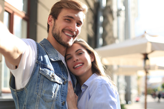 Beautiful lovely young couple walking at the city streets, hugging while taking a selfie.