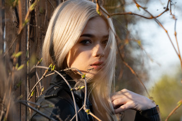 Naklejka premium A young beautiful blonde girl poses next to branches with green buds in early spring. Close-up portrait