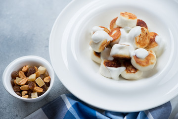 Close-up of roasted vareniki or dumplings made of cottage cheese and served with sour cream, selective focus, studio shot