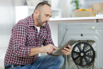 man looking at tablet by broekn down washing machine