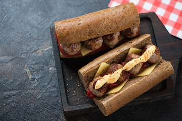 Wooden serving tray with two submarine meatball and cheese sandwiches, studio shot over dark brown stone background