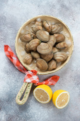 Serving pan with fresh uncooked iced vongole clams and lemon, above view on a beige stone background, vertical shot