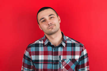 Fototapeta premium The guy in the plaid shirt on the red background. Emotions on the face.