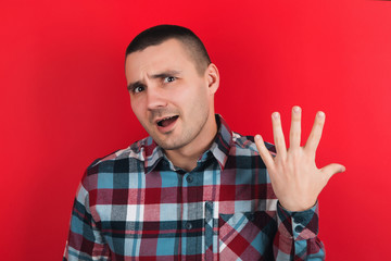 Fototapeta premium The guy in the plaid shirt on the red background. Emotions on the face.