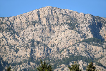 Landscape with high impregnable mountains with poor vegetation on the slopes under blue cloudless sky on bright sunny day front view horizontal