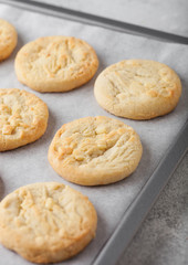 White chocolate biscuit cookies on baking tray on light kitchen table background.